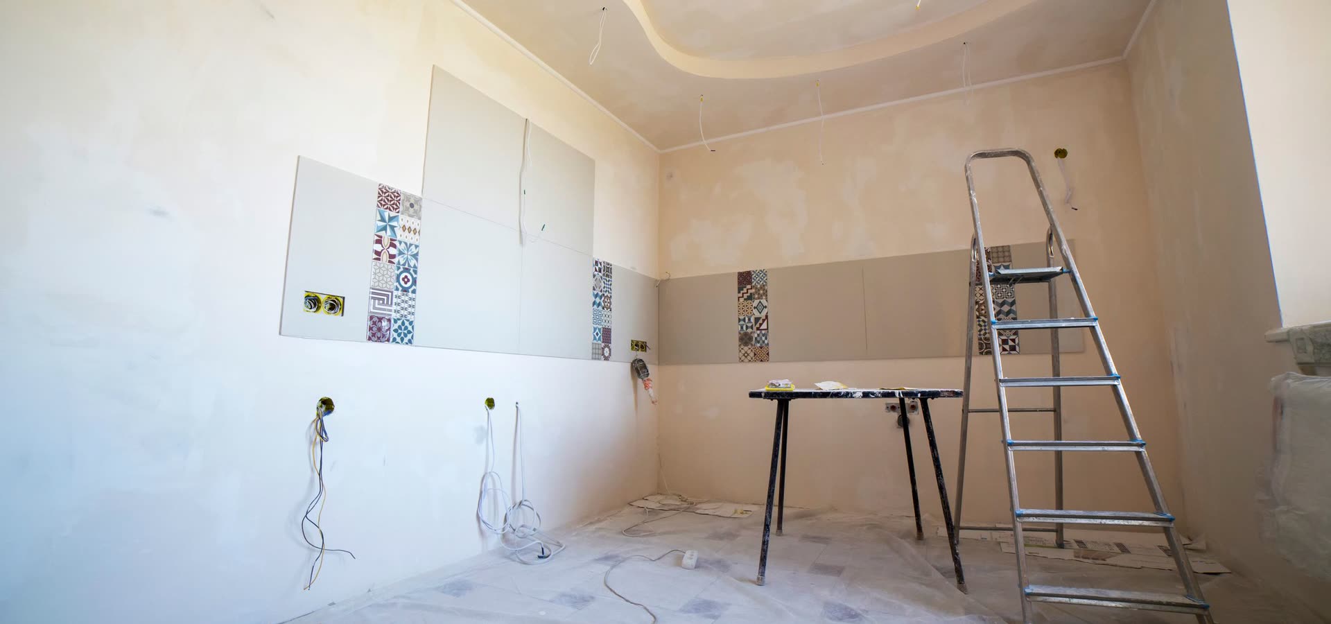 Ett rum mitt i en renovering med stege, plast på golvet och uppsatta kakelprover.