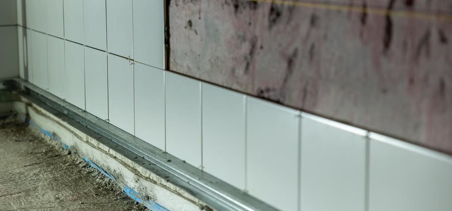 Vitt kakel satt halvvägs upp på en badrumsvägg, med kryss kvar i fogarna och tätskiktet synligt ovanför.